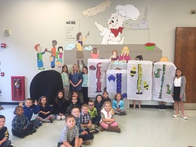 Group of children and adults posing in a room with cartoon wall art
