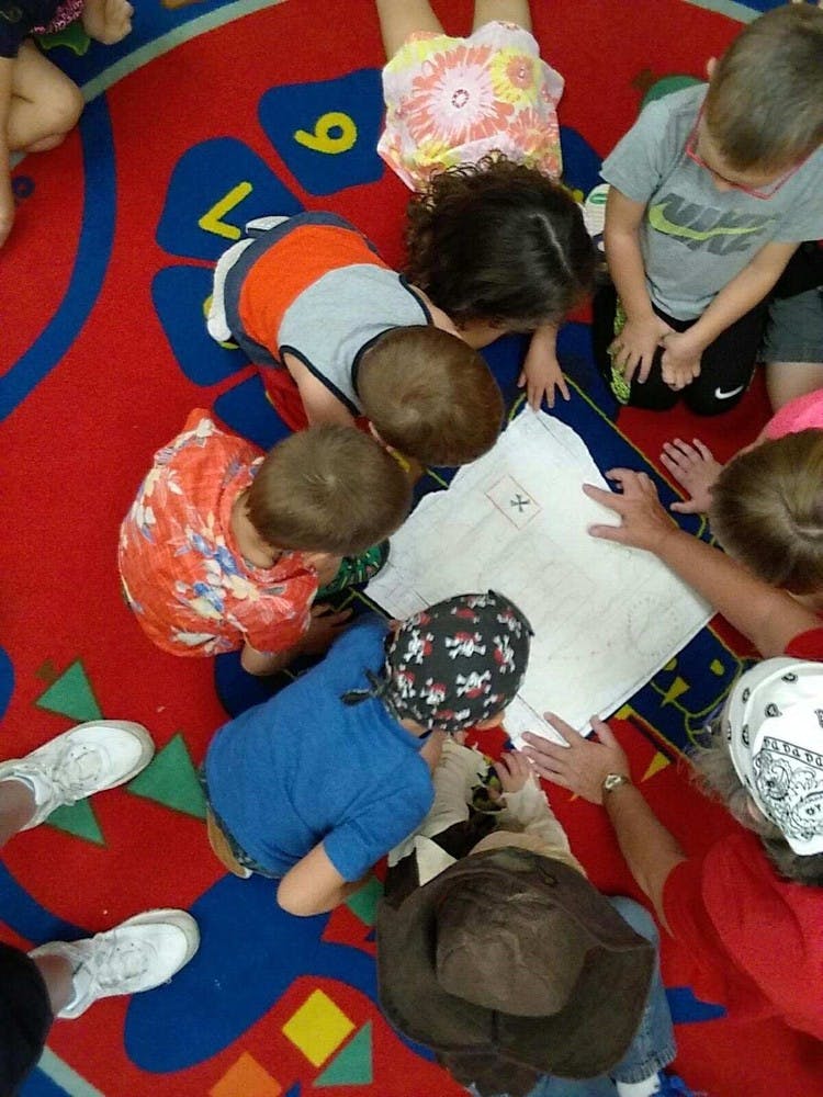 Children and adults looking at a map on a colorful rug