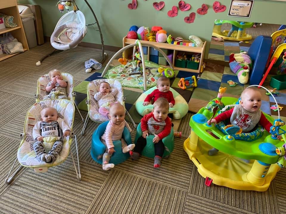 Multiple babies sitting in various chairs and play equipment in a room