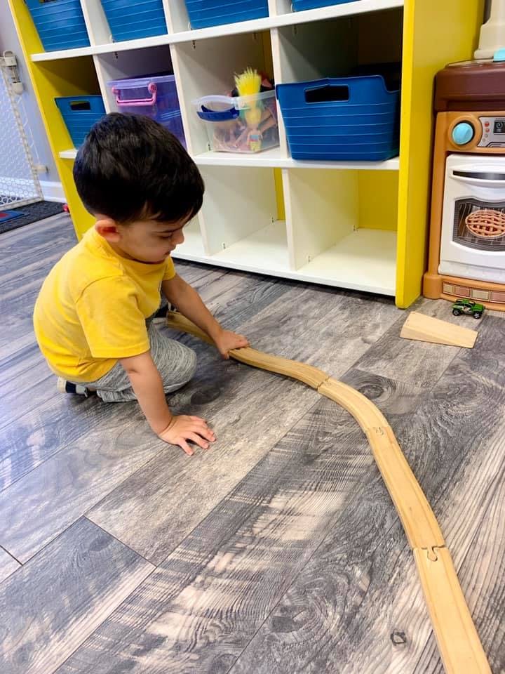 Child playing with a wooden train track on the floor