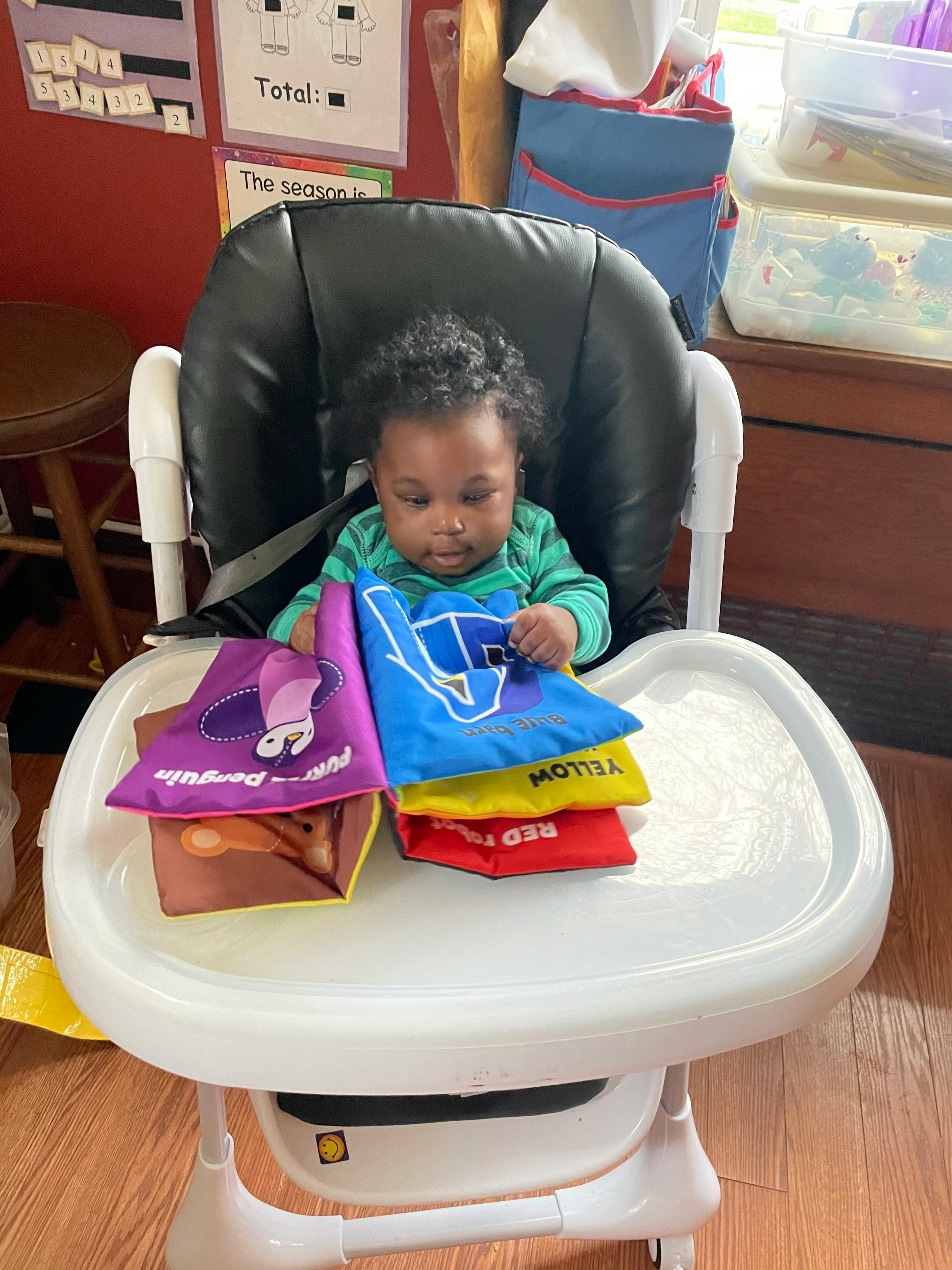 Child in a high chair playing with a soft book