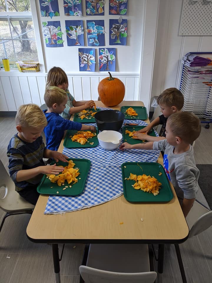Children at a table scooping pumpkin guts onto green trays