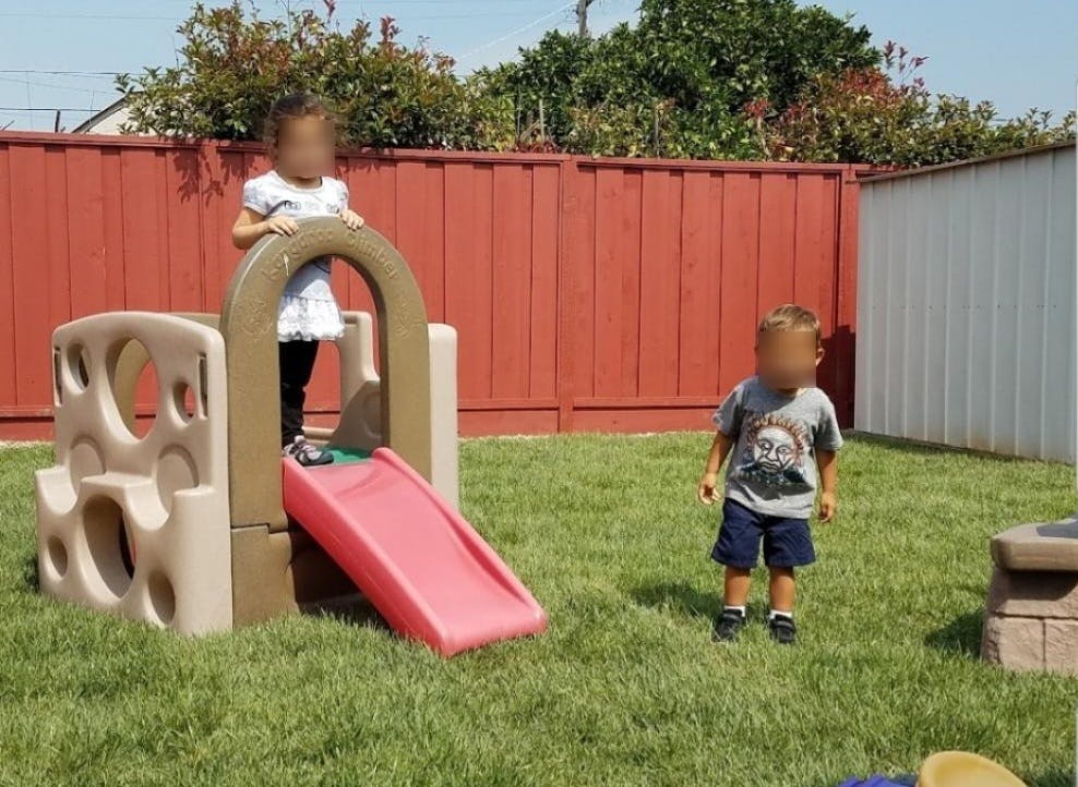 Child standing on a play structure with a slide, another child standing nearby