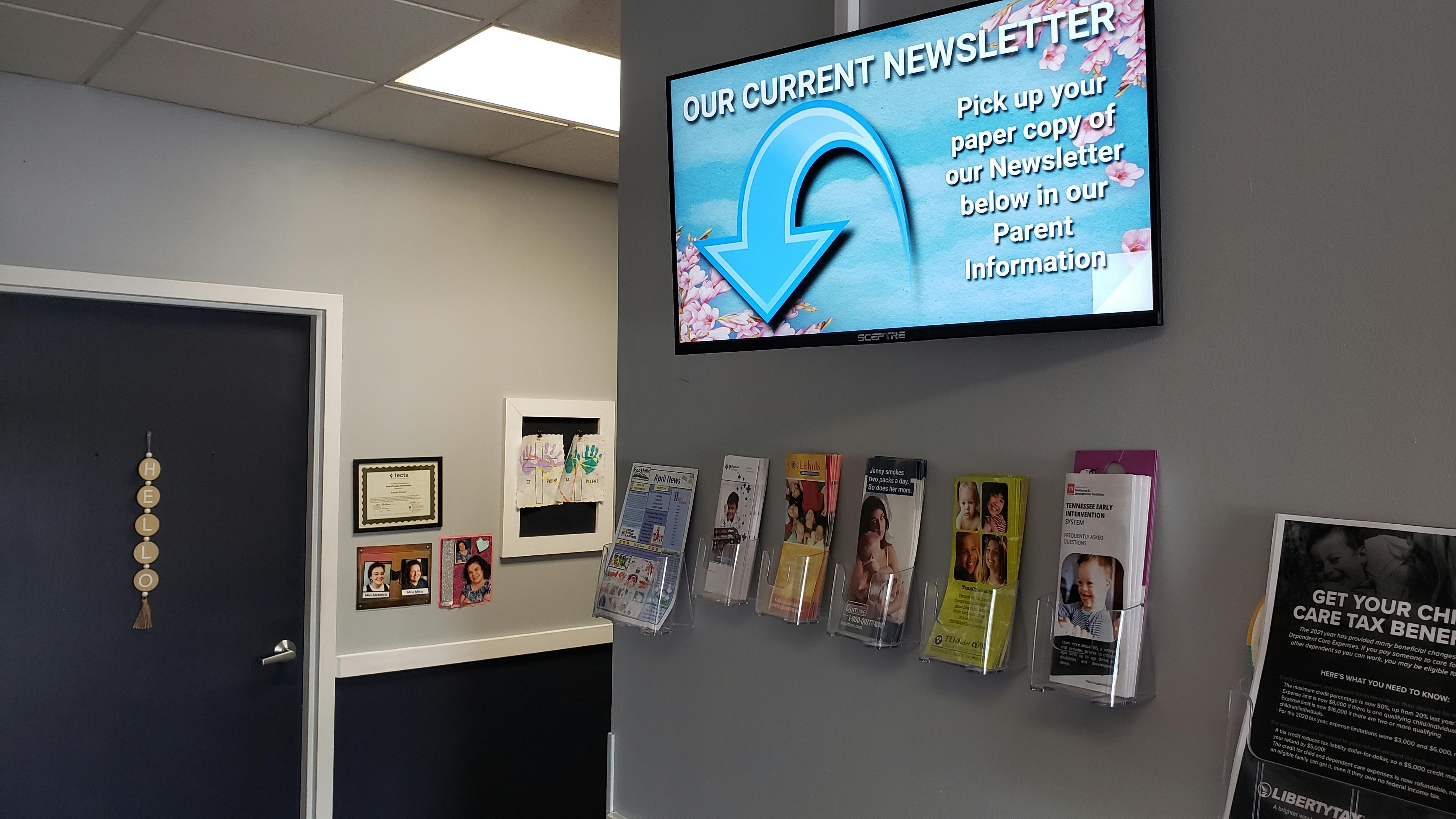 Wall with a digital display showing "OUR CURRENT NEWSLETTER" and brochures