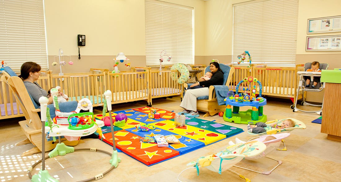 Two people with children in a nursery room with cribs and playmats
