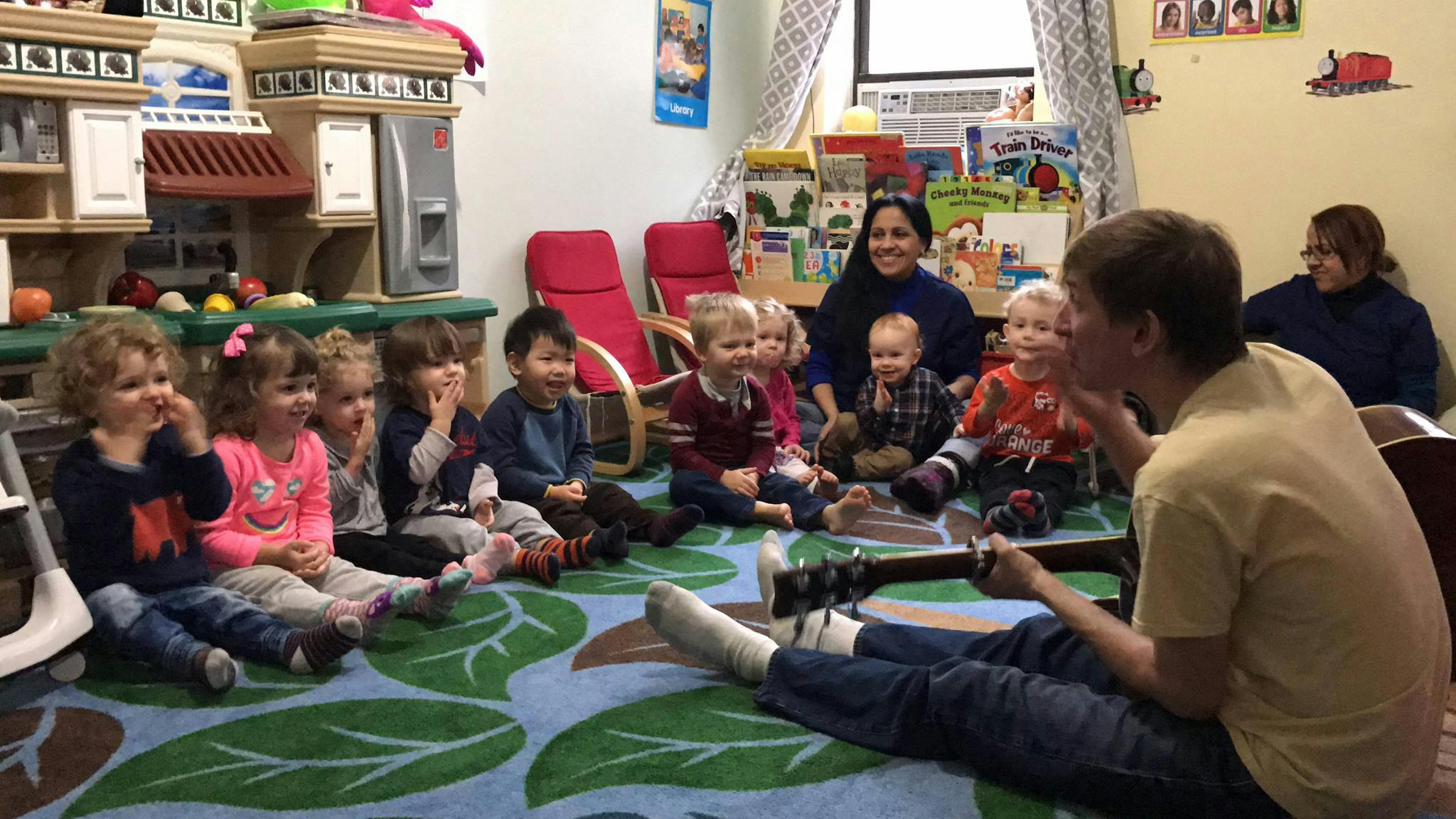 Adult playing guitar for a group of children and adults in a classroom