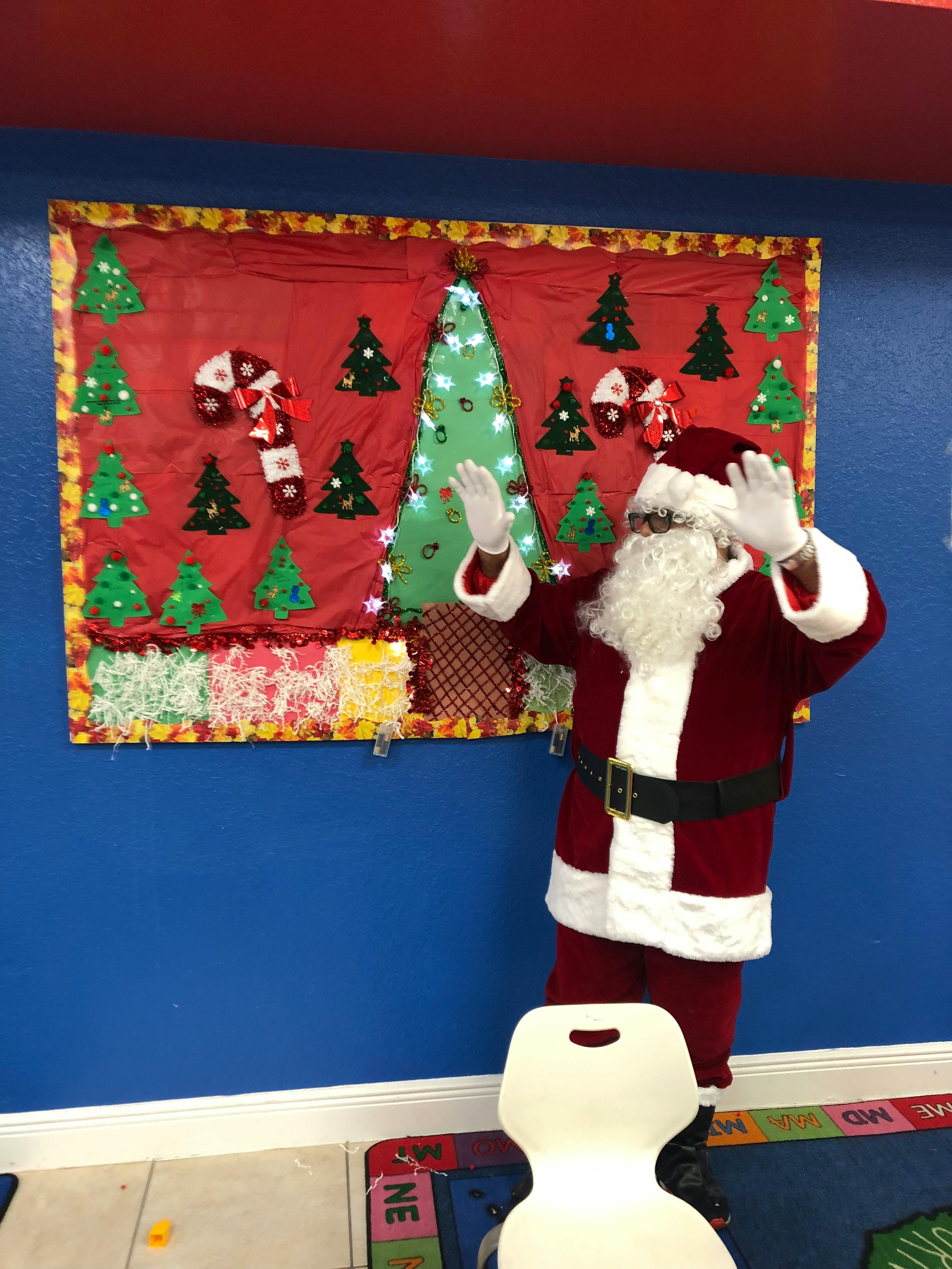Person in Santa costume with arms raised in front of a Christmas decoration