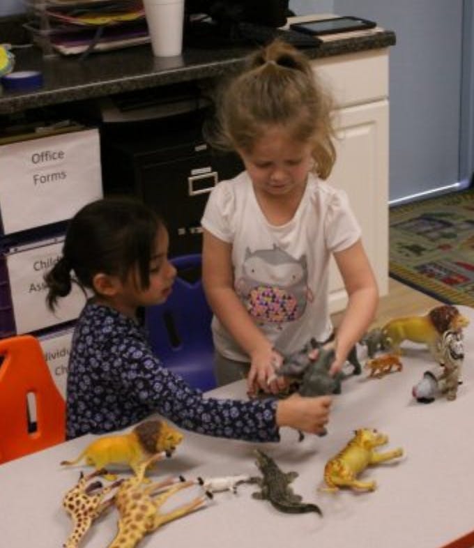 Two children playing with animal figurines on a table