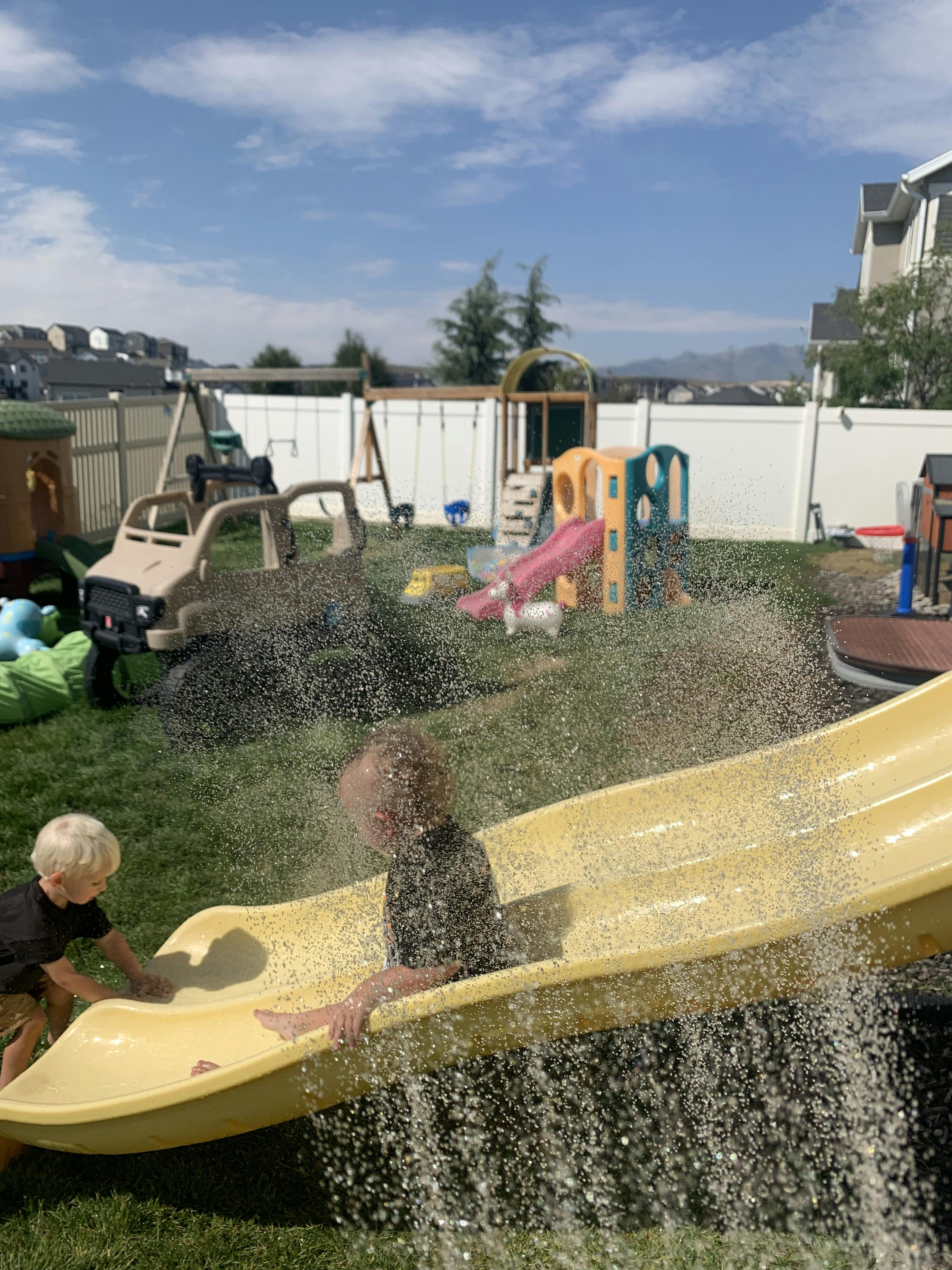 Two children playing on a yellow slide with water spraying