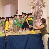Adult helping child in graduation cap and gown on stage with other children