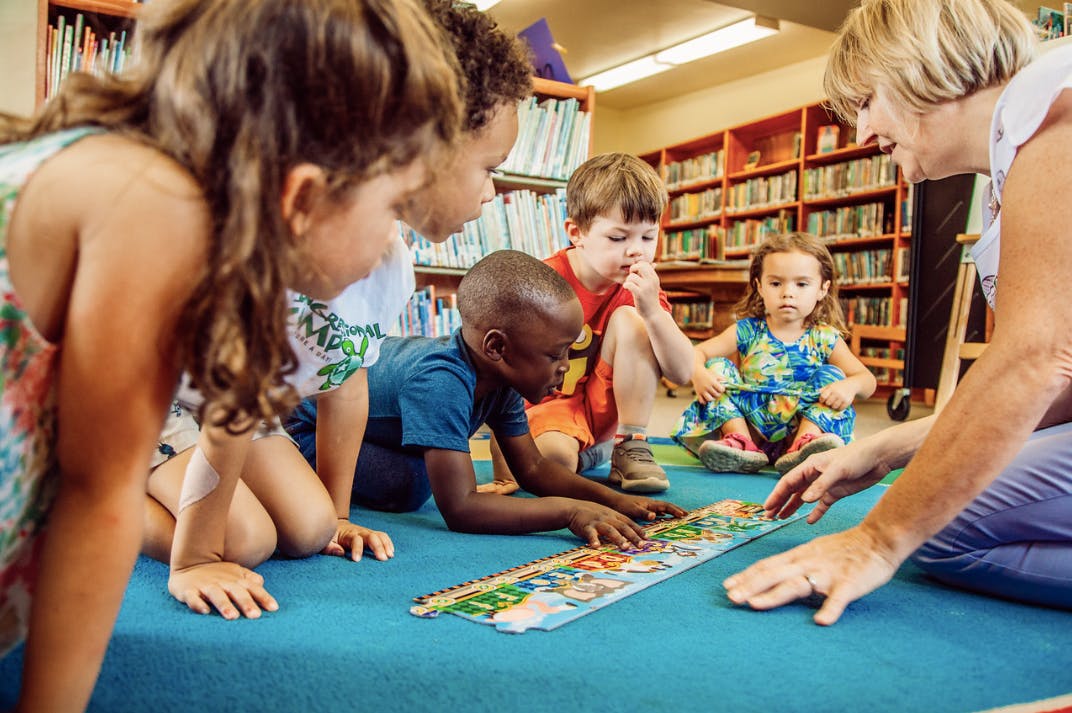 Adult and children on floor playing with puzzle in a library