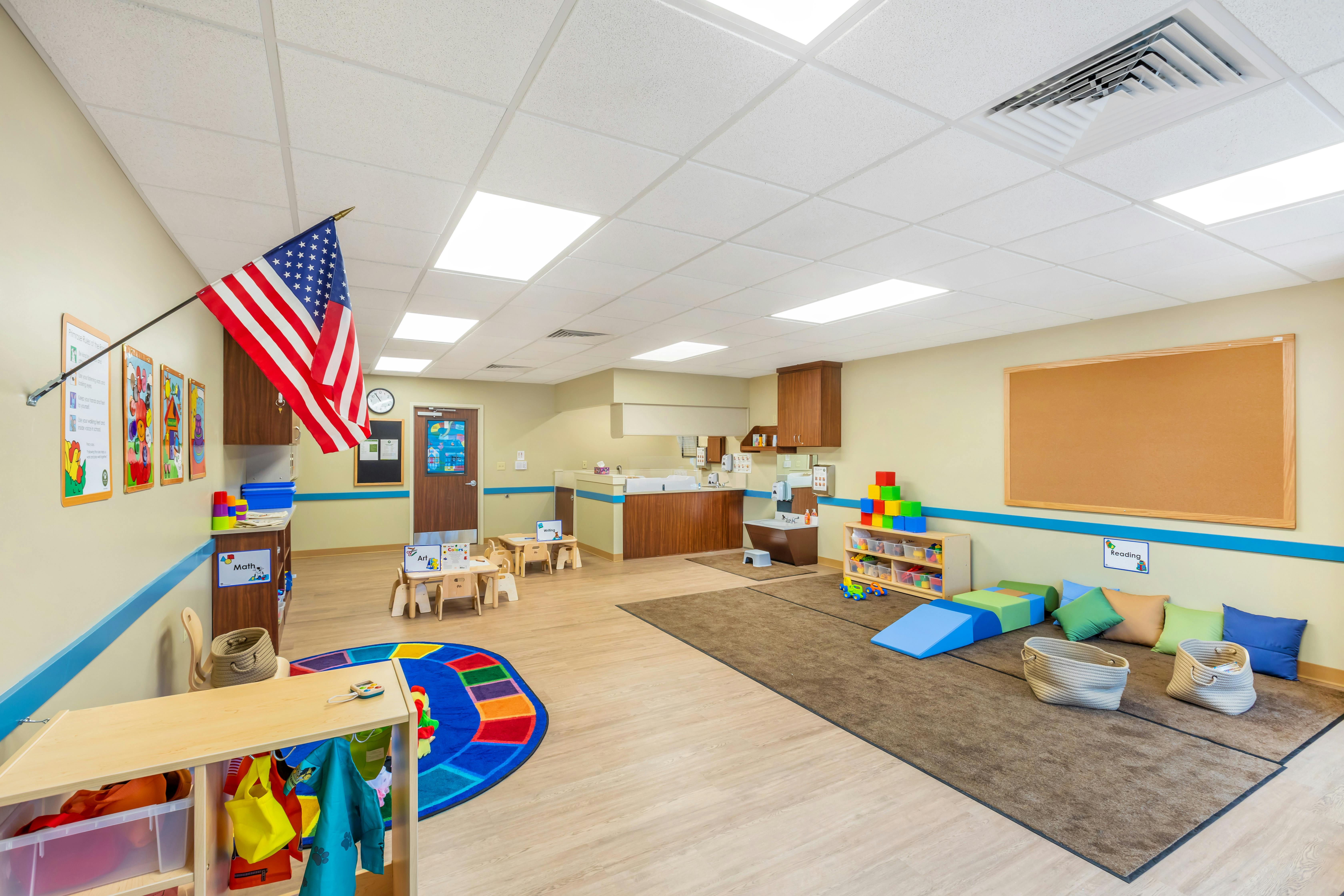 Classroom with child-sized tables and chairs, a reading corner, and a sensory play area