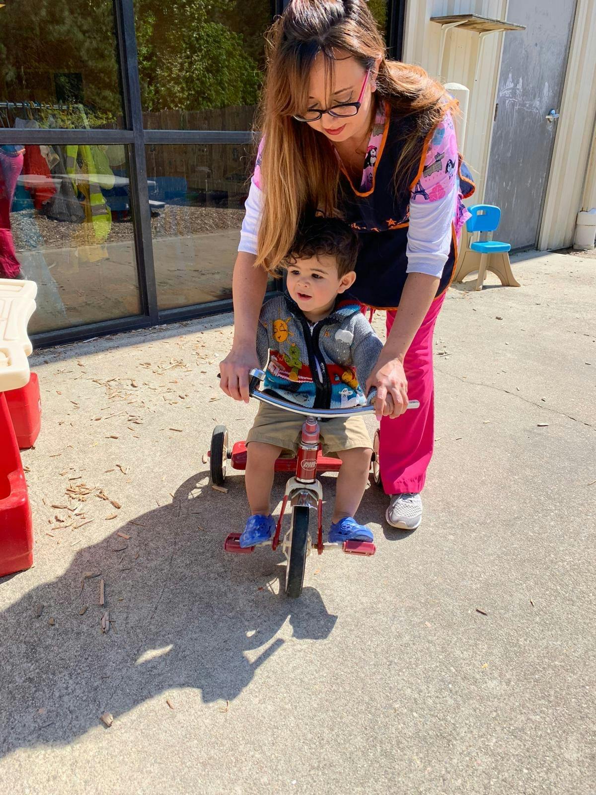 Person helping a child ride a tricycle outdoors