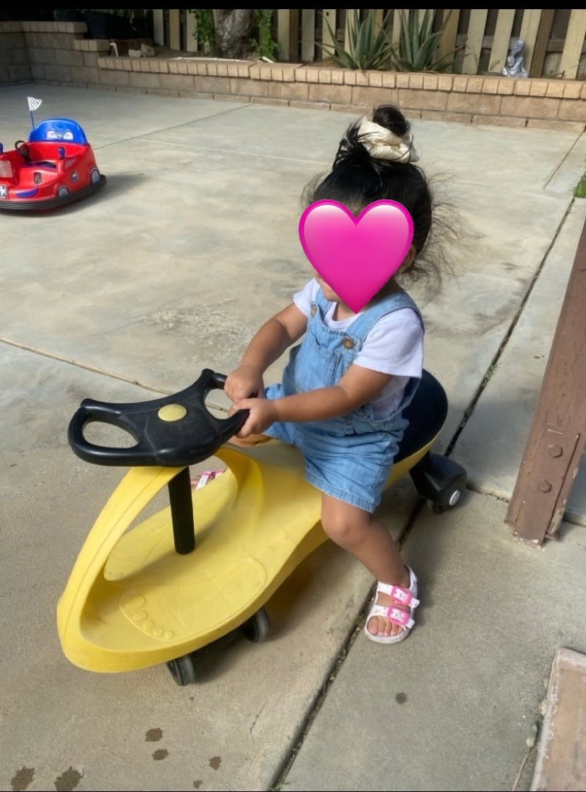 Child sitting on a yellow toy ride-on car on a patio