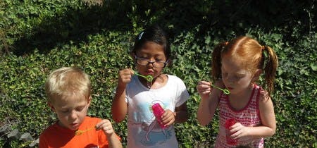 Three children blowing bubbles outdoors