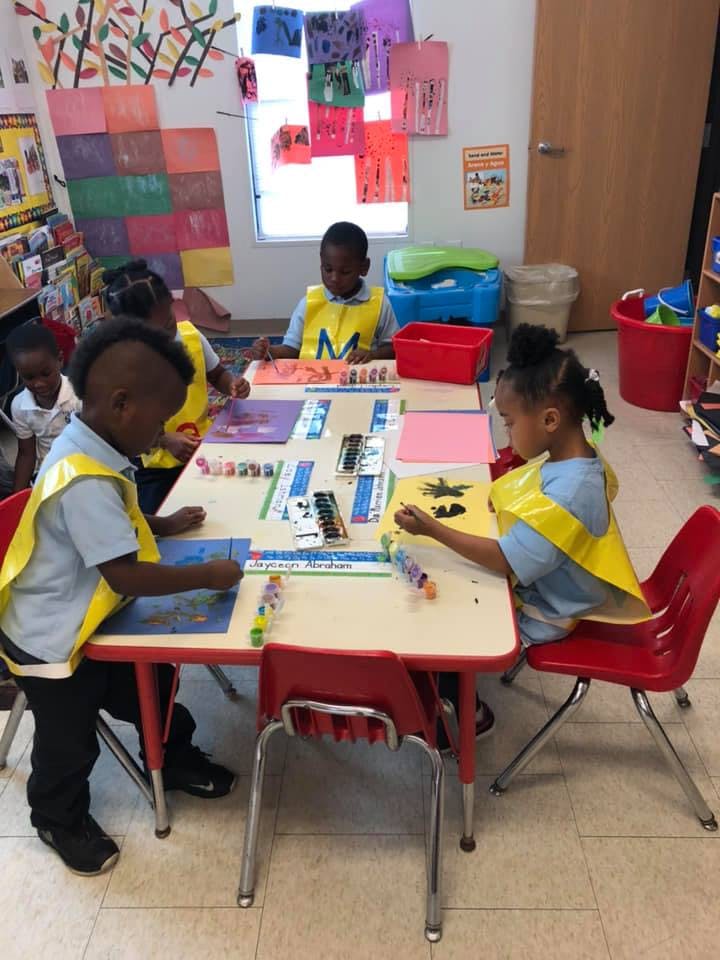 Children in yellow vests doing crafts at a table in a classroom