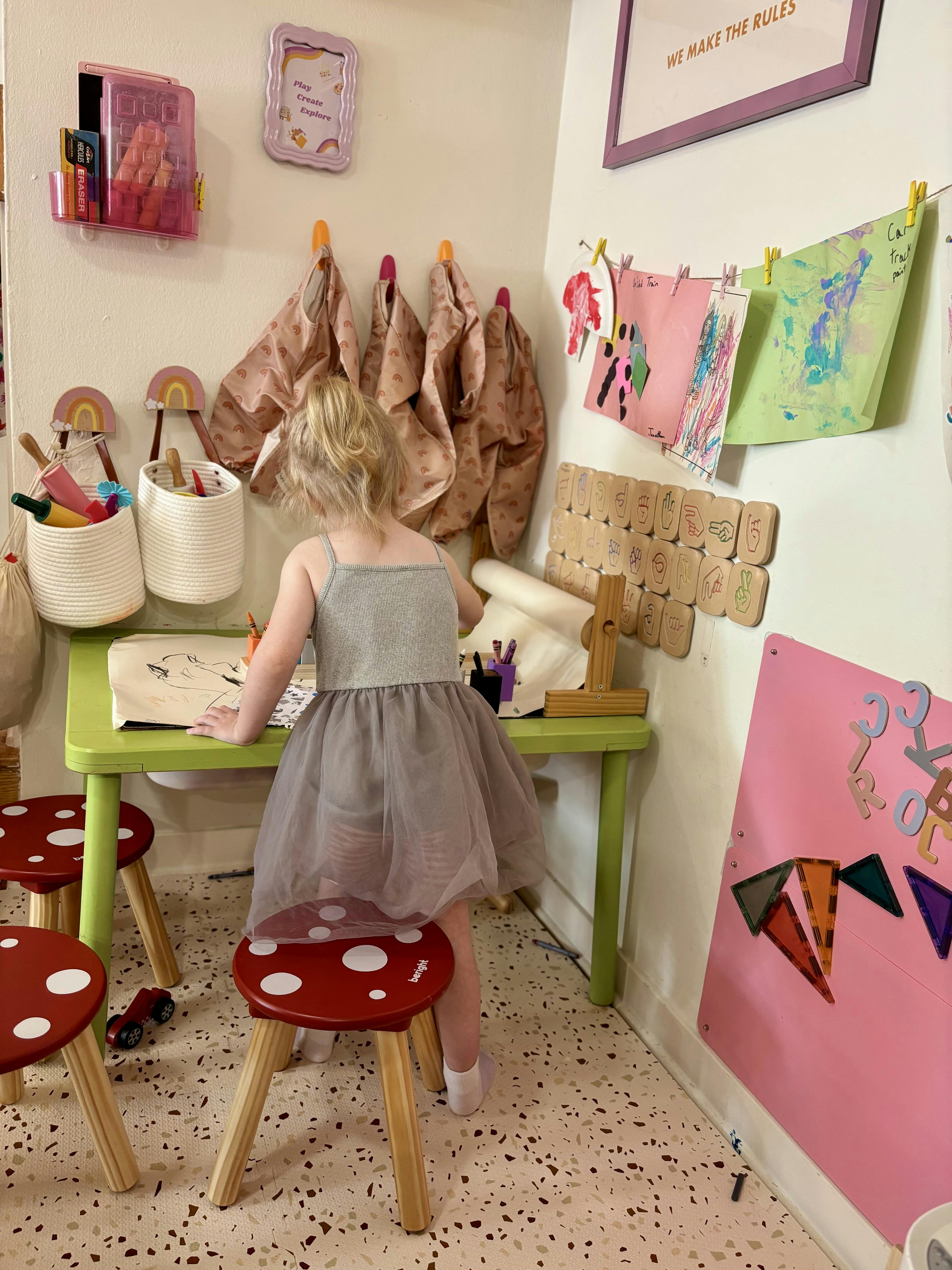 Child standing at a small green table with art supplies