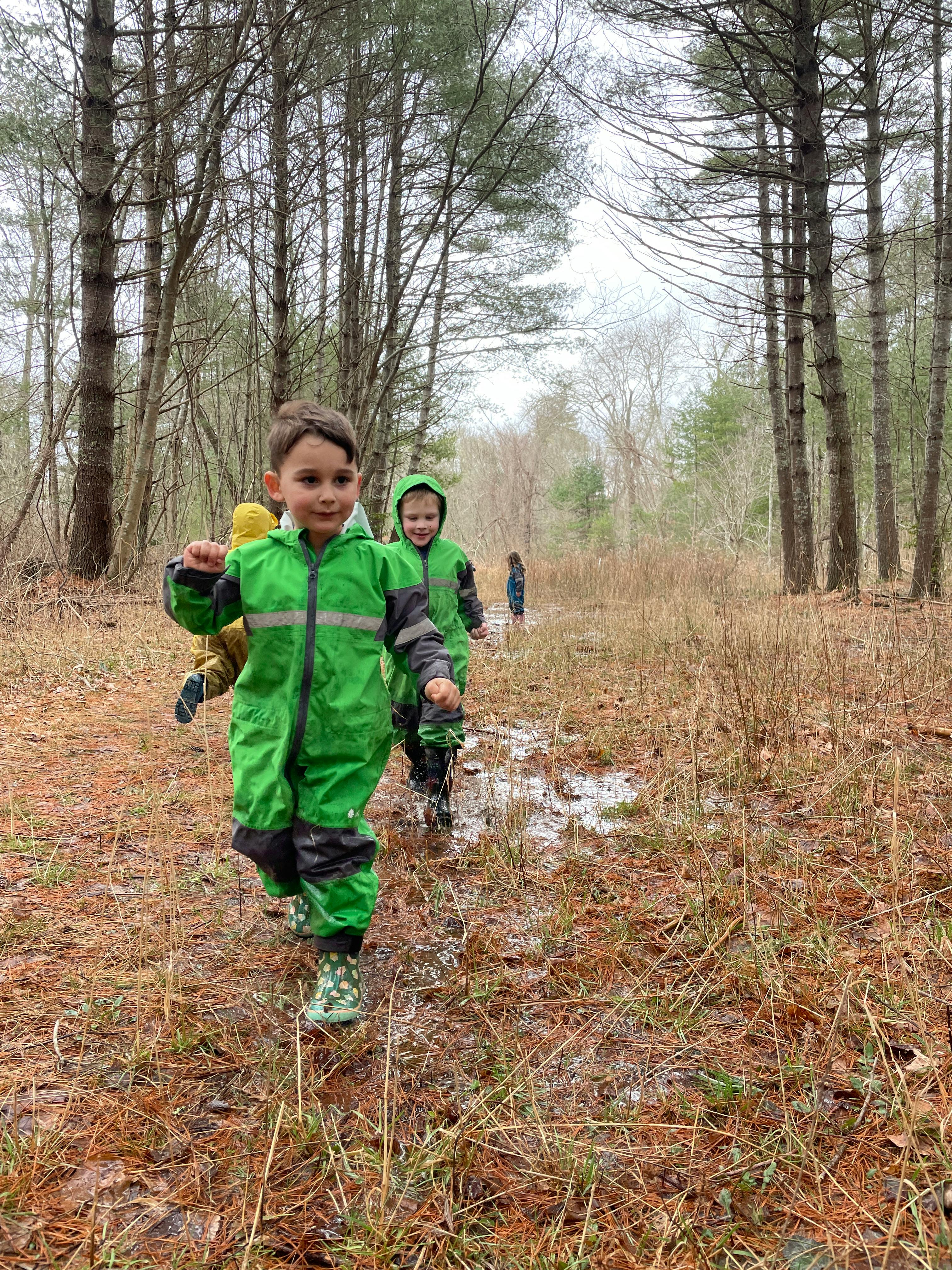 Children in green rain suits walking through a muddy forest