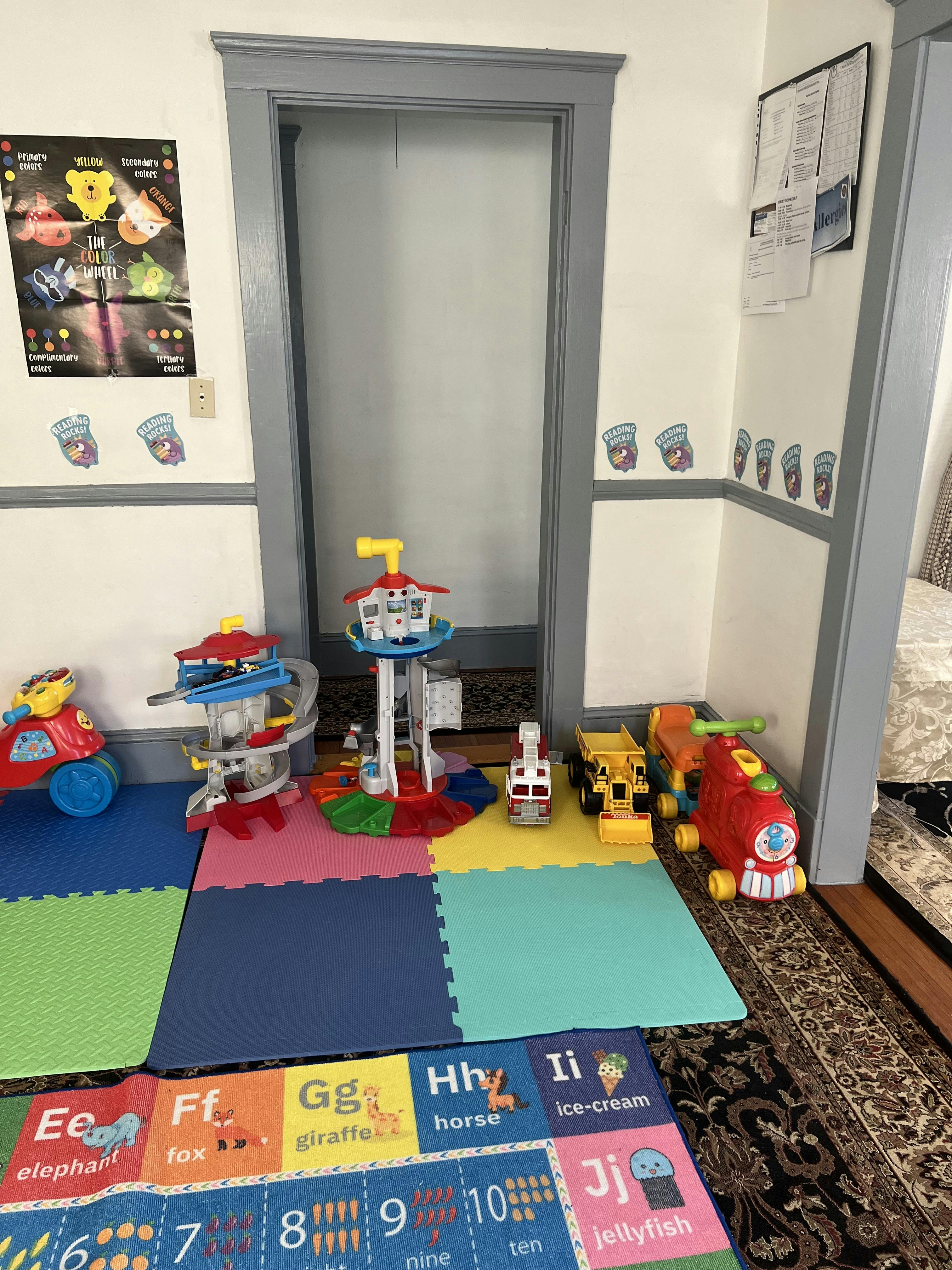 A playroom with colorful playmats and several children's toys, including a fire truck and a train
