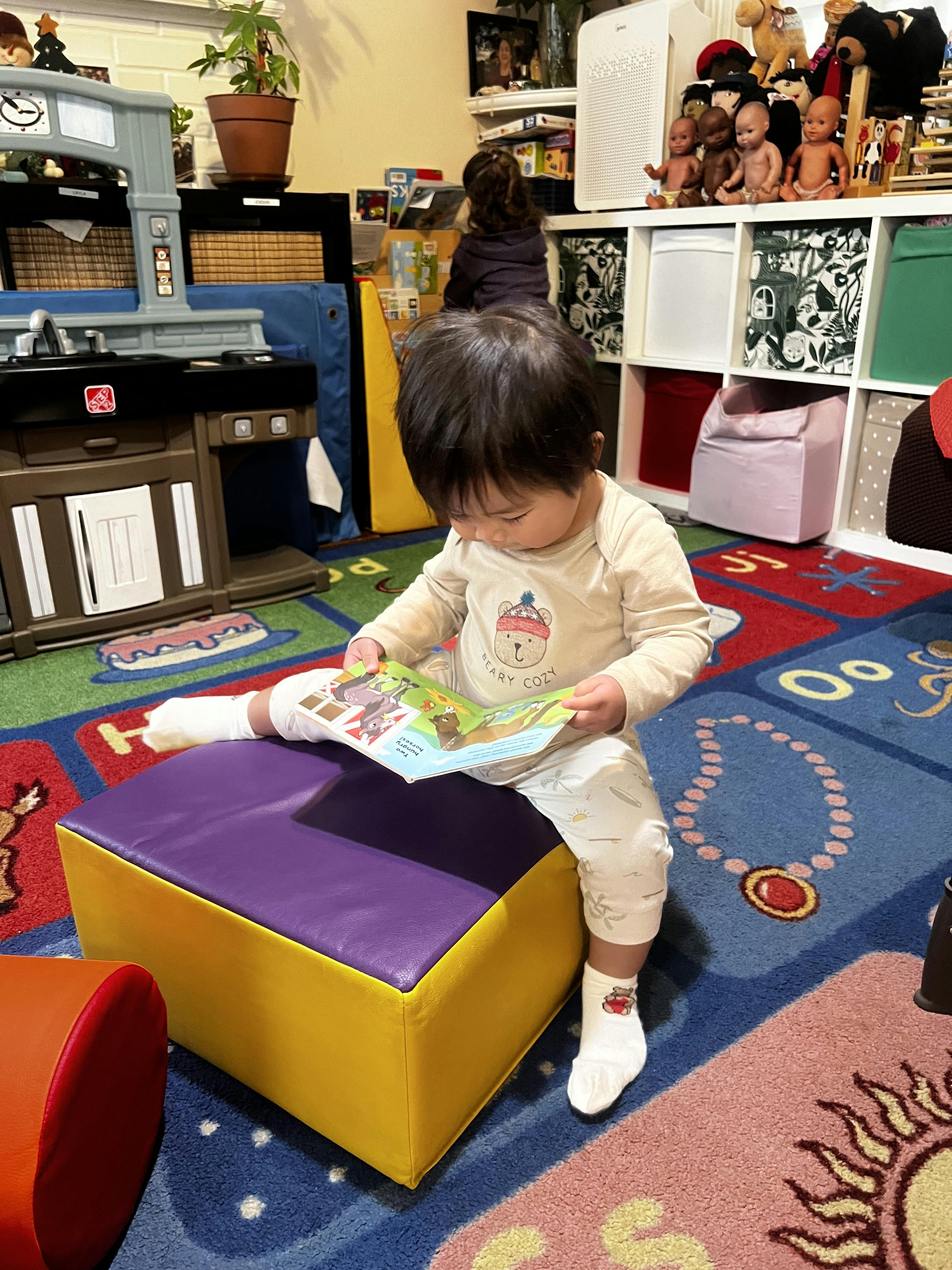 Child sitting on a purple and yellow block, reading a book