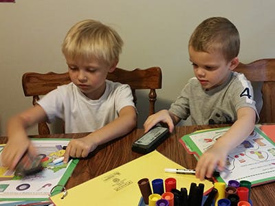 Two children sitting at a table with papers and markers