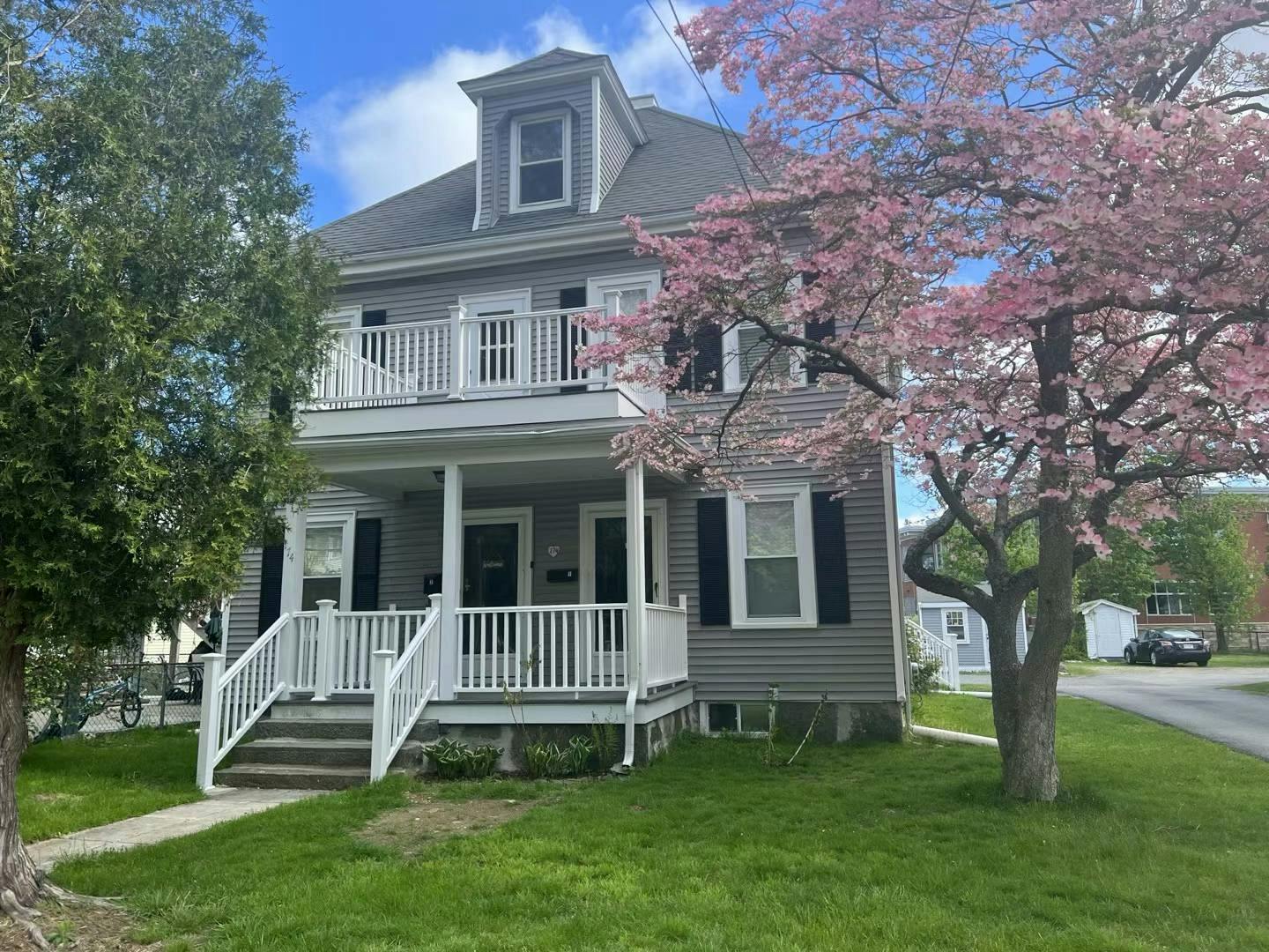 Gray house with white porch and balcony, pink flowering tree
