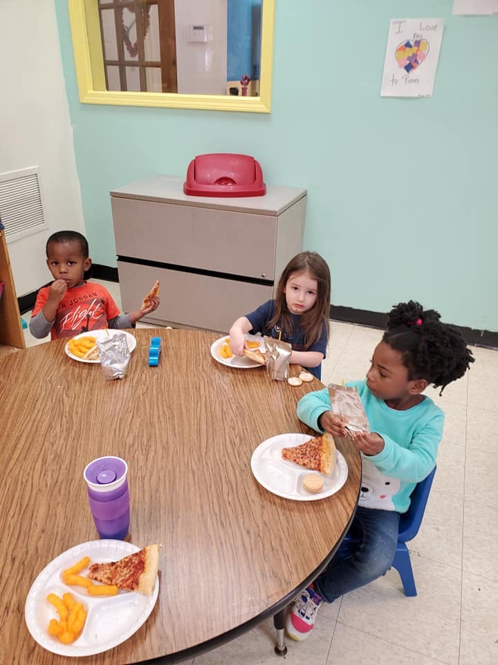 Three children eating pizza and snacks at a round table