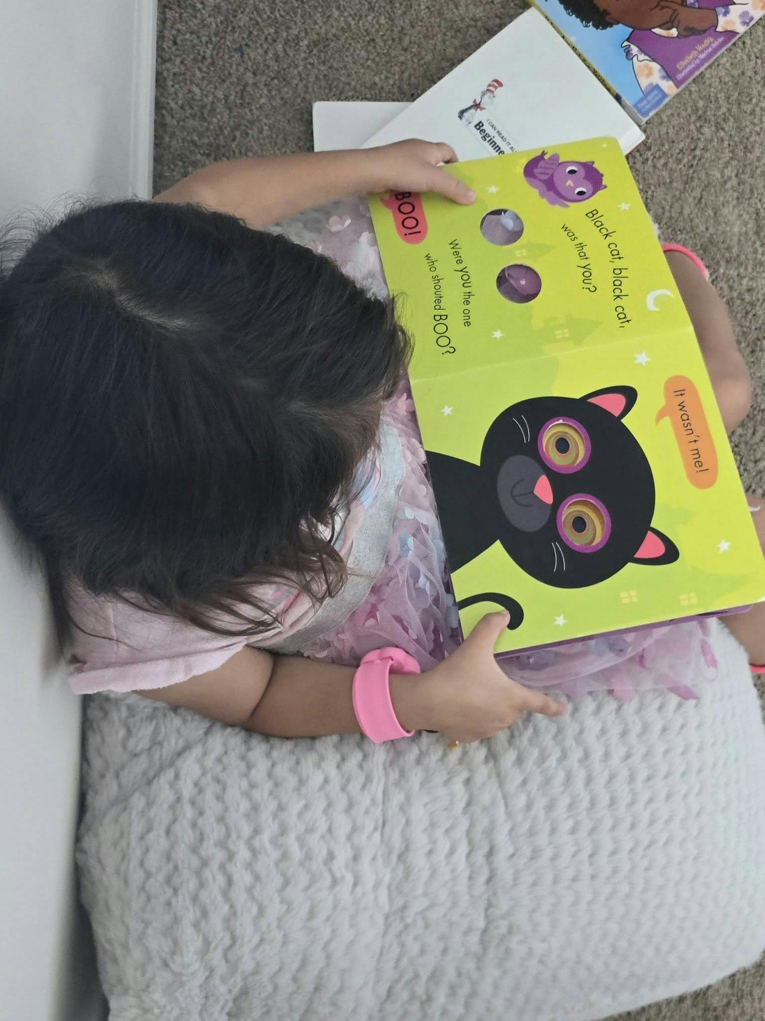 Child sitting and reading a book about a black cat