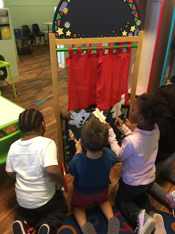 Three children playing with puppets behind a puppet theater