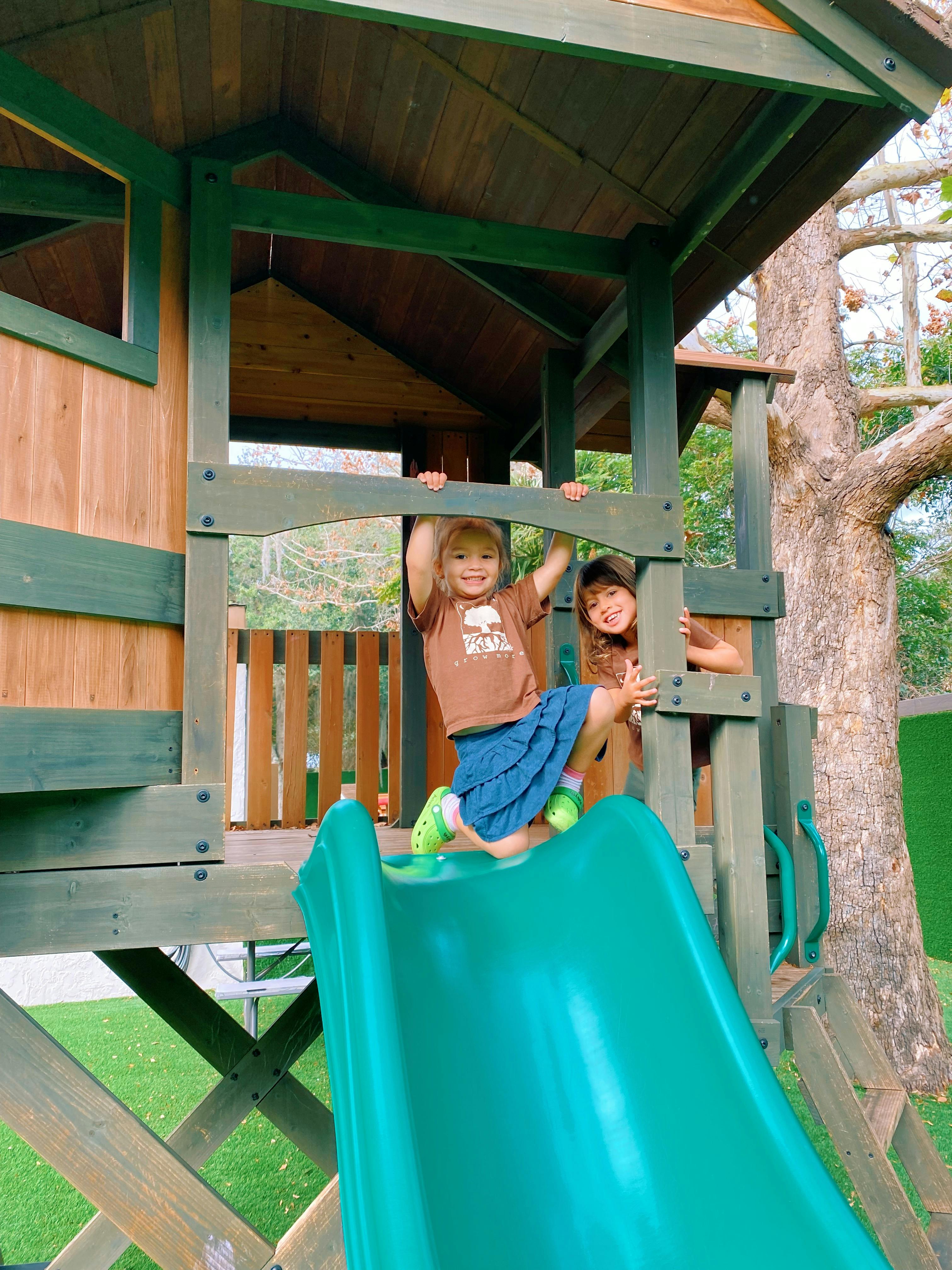 Two children on a wooden play structure with a green slide