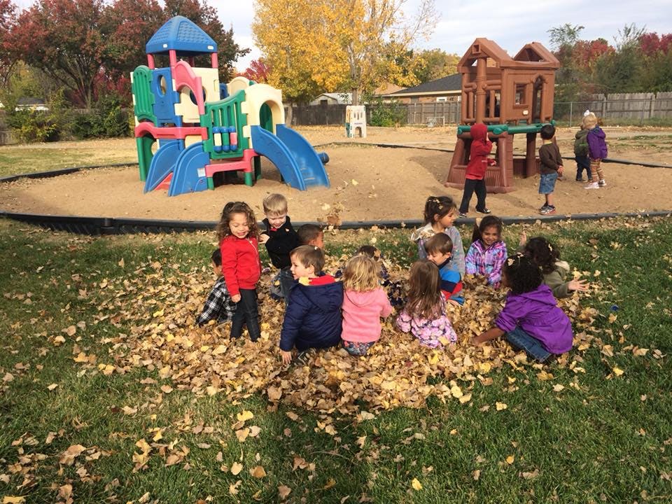 Children playing in a pile of autumn leaves on a playground