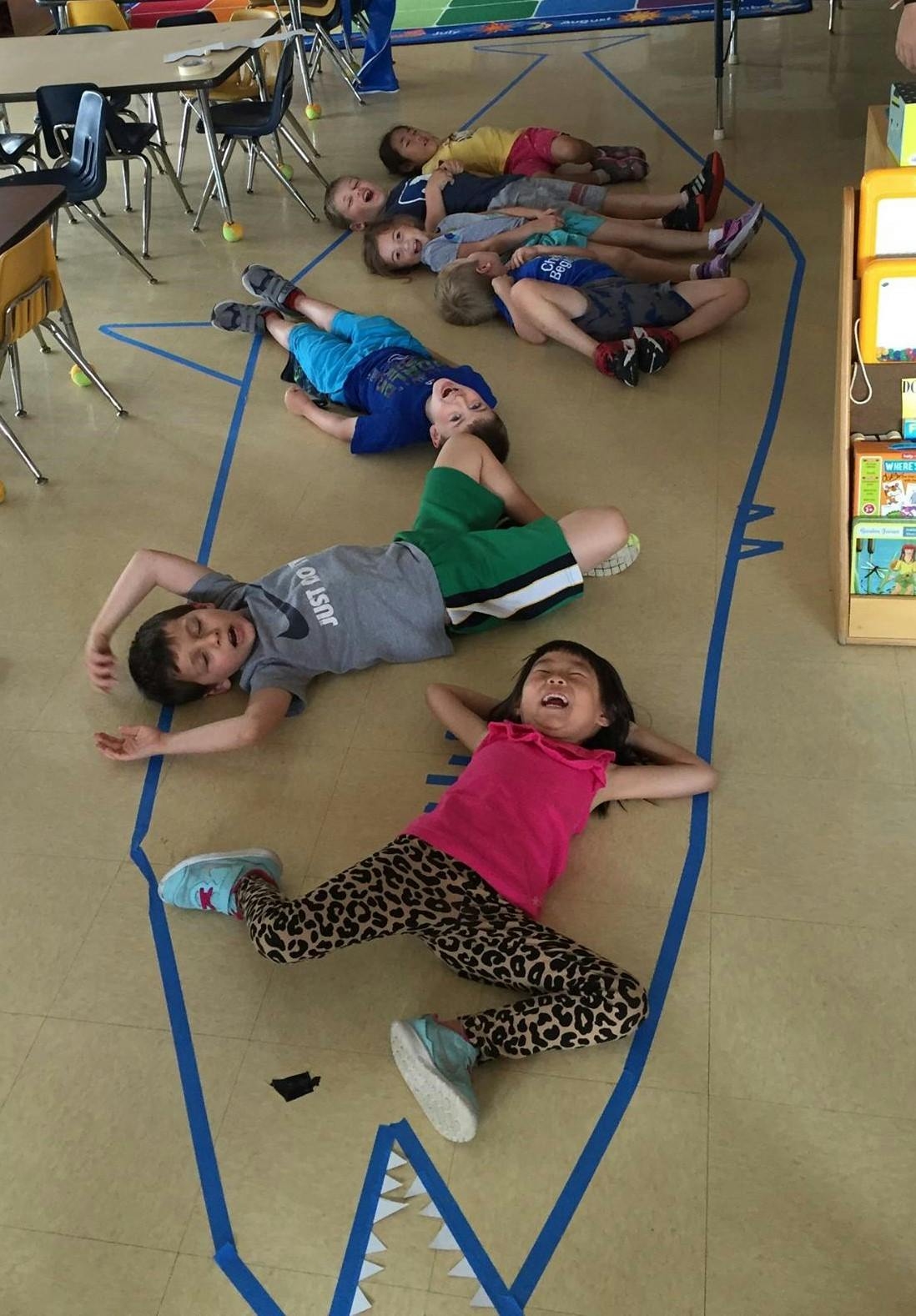 Children lying on the floor inside a blue tape outline of a shark
