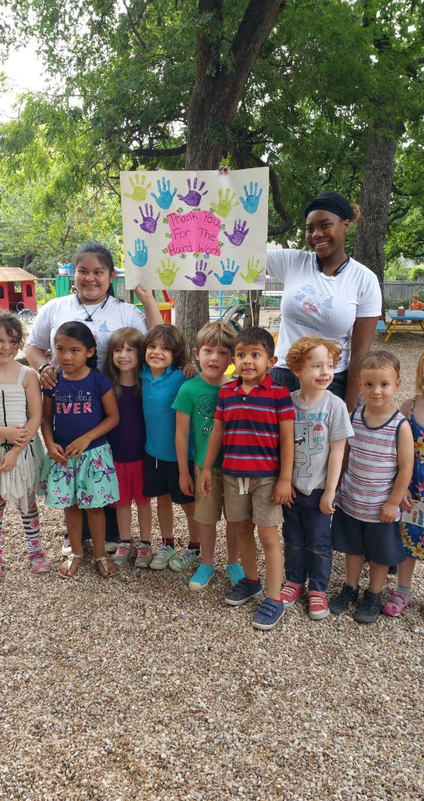 Two adults and a group of children holding a sign with handprints