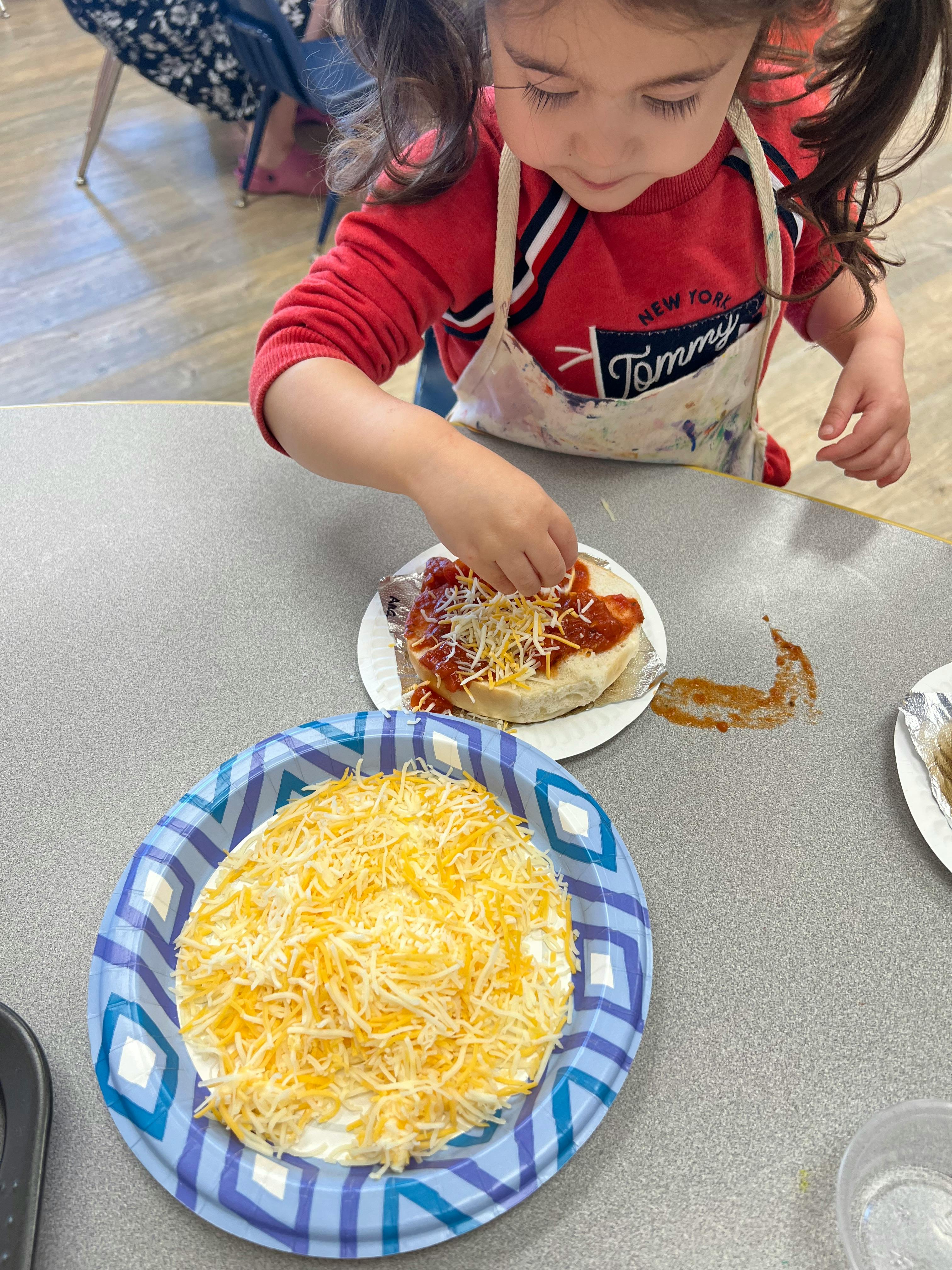 Child adding shredded cheese to food on a plate