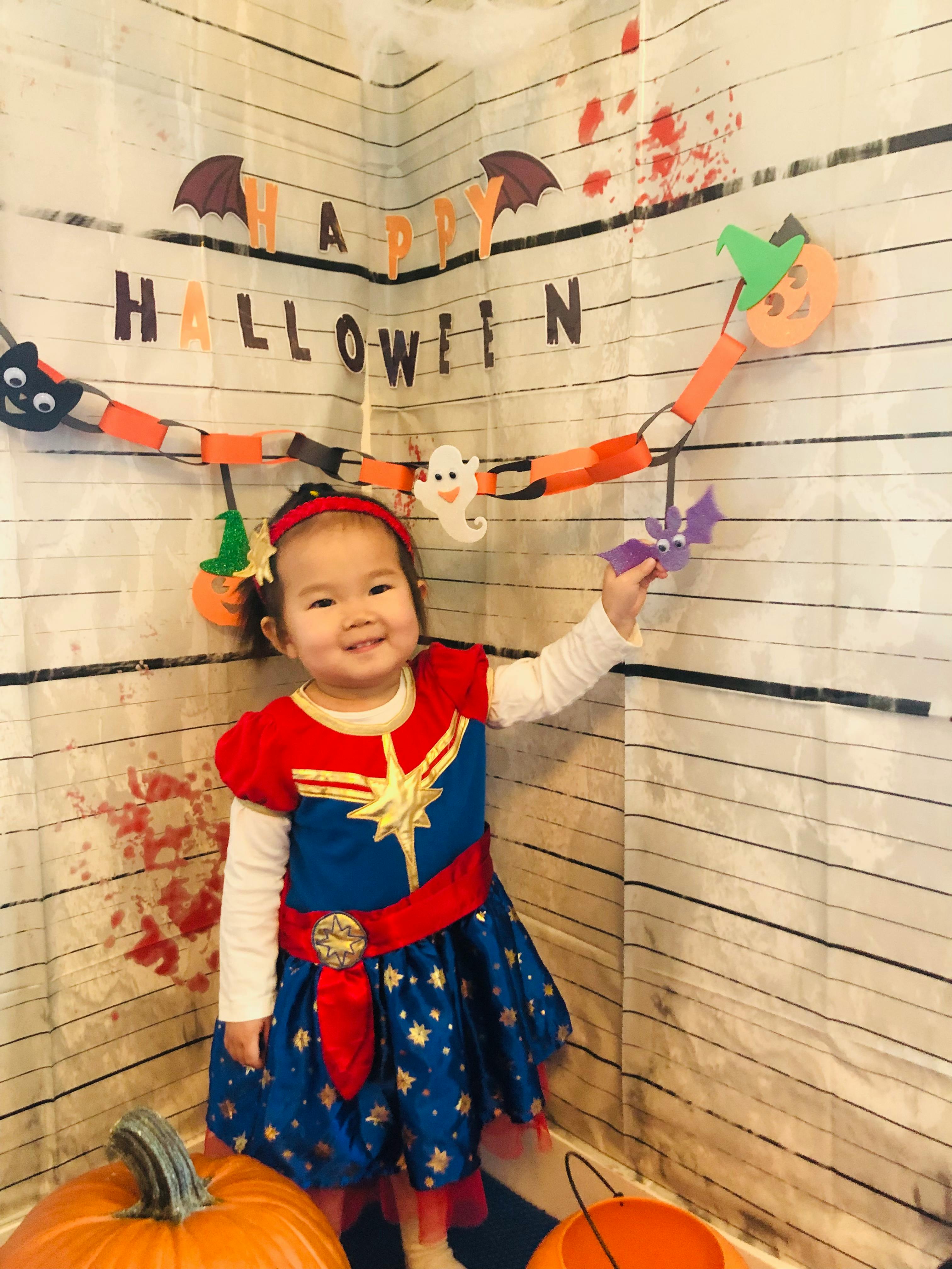 Child in a Captain Marvel costume holding a bat decoration