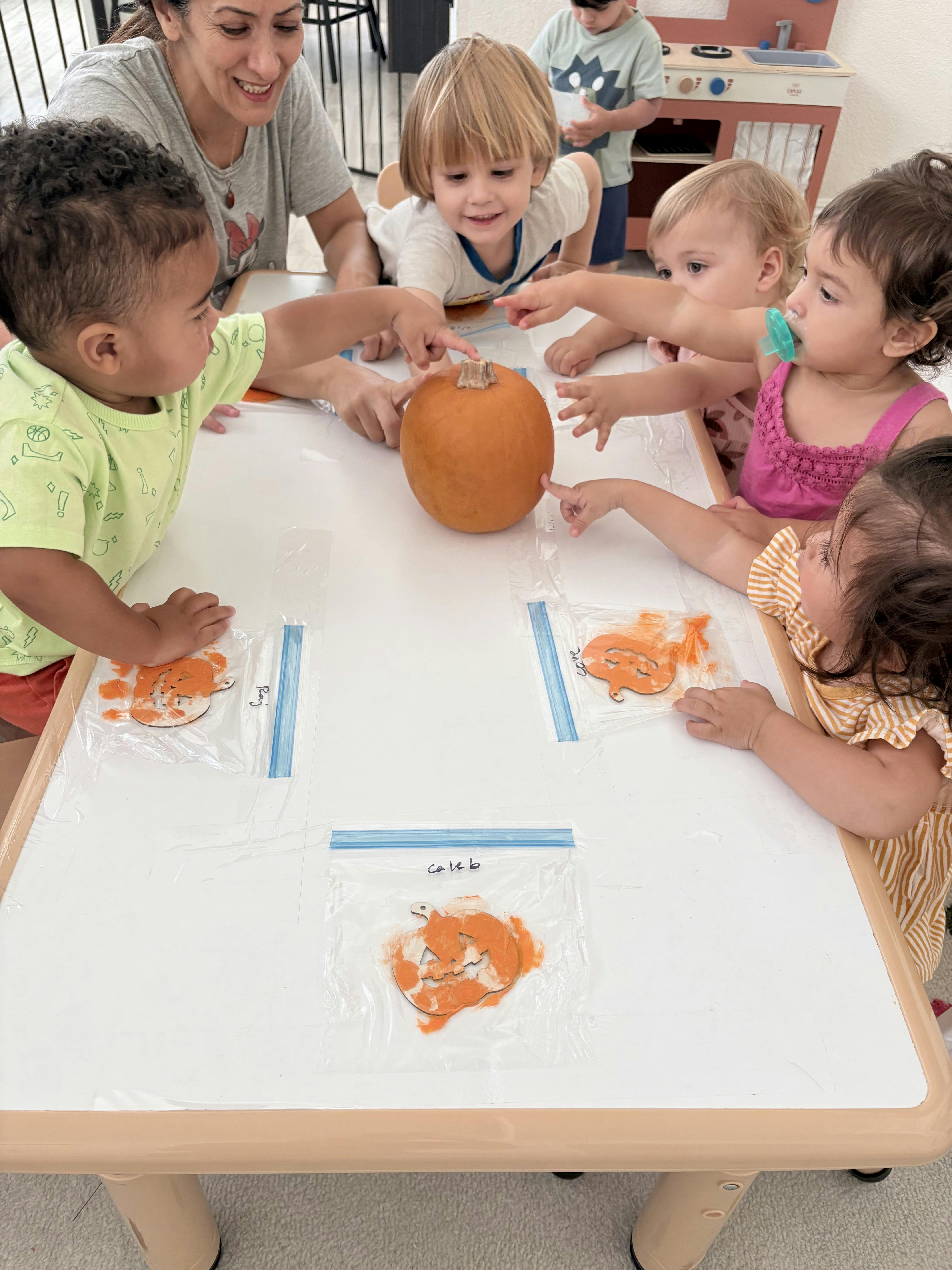 Group of children and an adult gathered around a table with a pumpkin