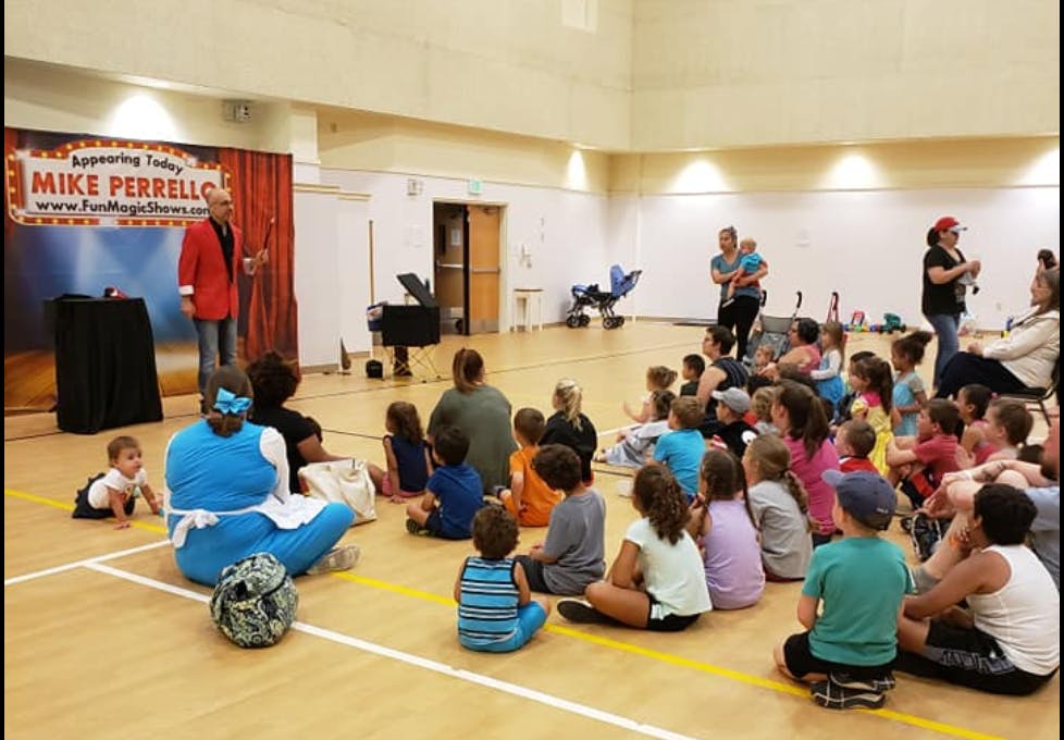 Person in red jacket performing for an audience of adults and children