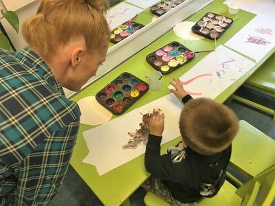 Person watching child paint at a table with paint palettes