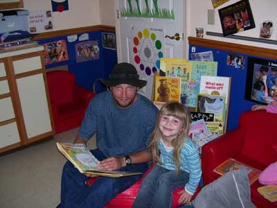 Person and child sitting on a red beanbag chair reading a book