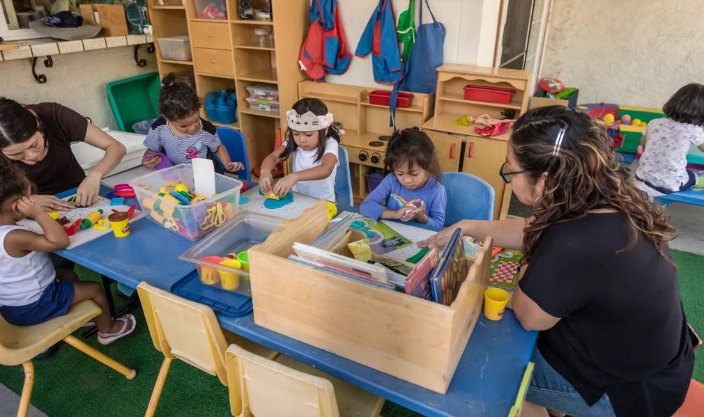 Adults and children playing with toys at a table in a classroom