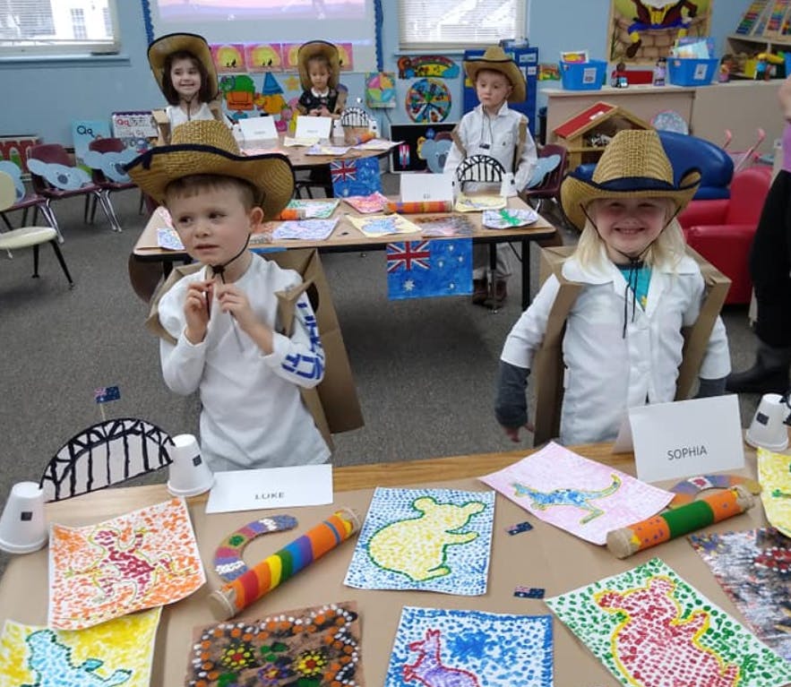 Children in cowboy hats and costumes standing behind tables with crafts