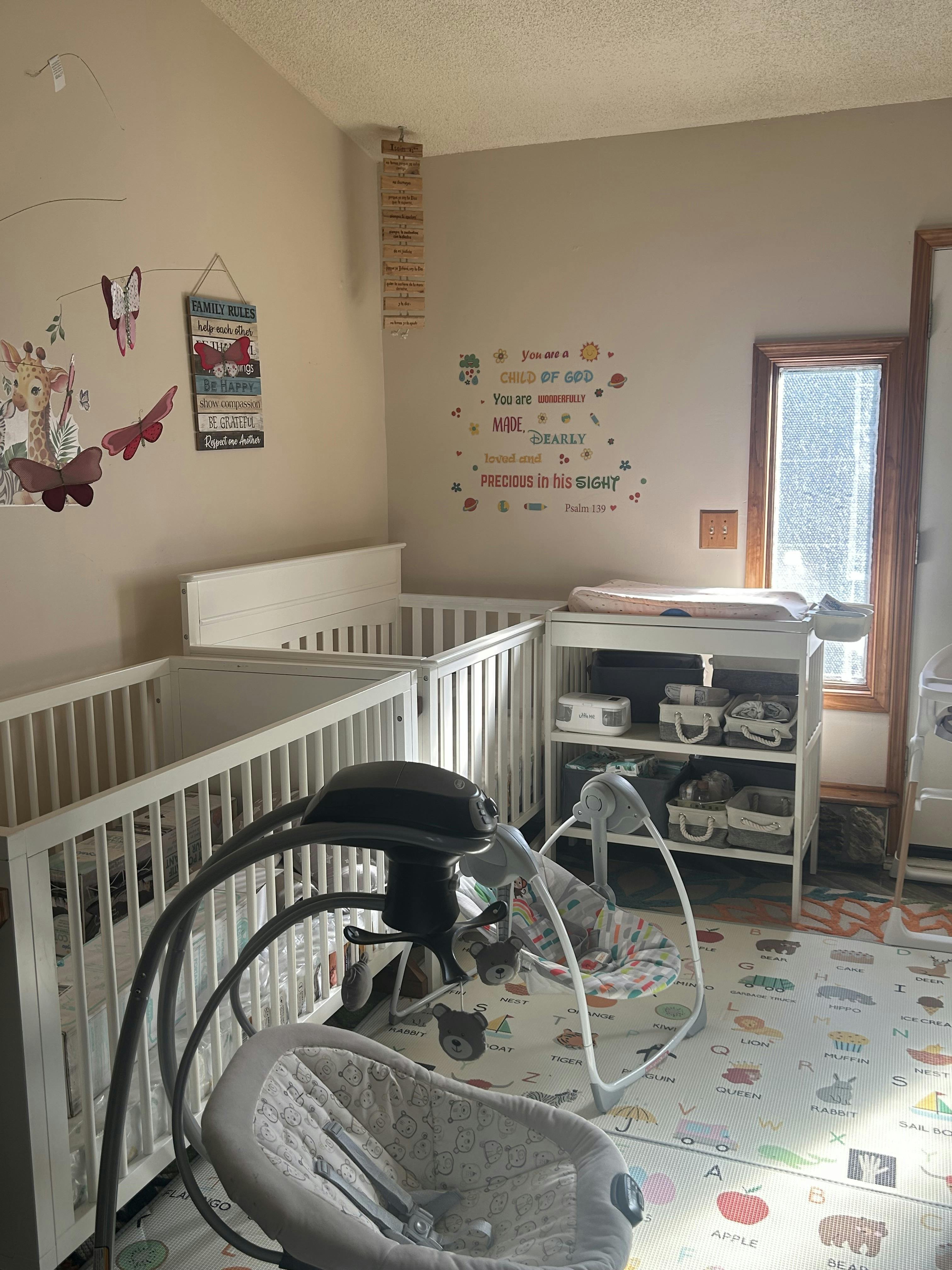 Baby nursery with two cribs, a changing table, and a baby swing on a play mat