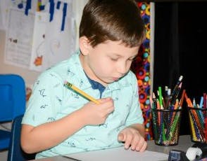 Child drawing with a pencil at a desk