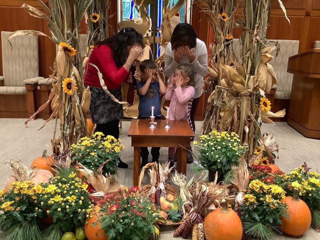 People and children with hands over eyes around a lit candle