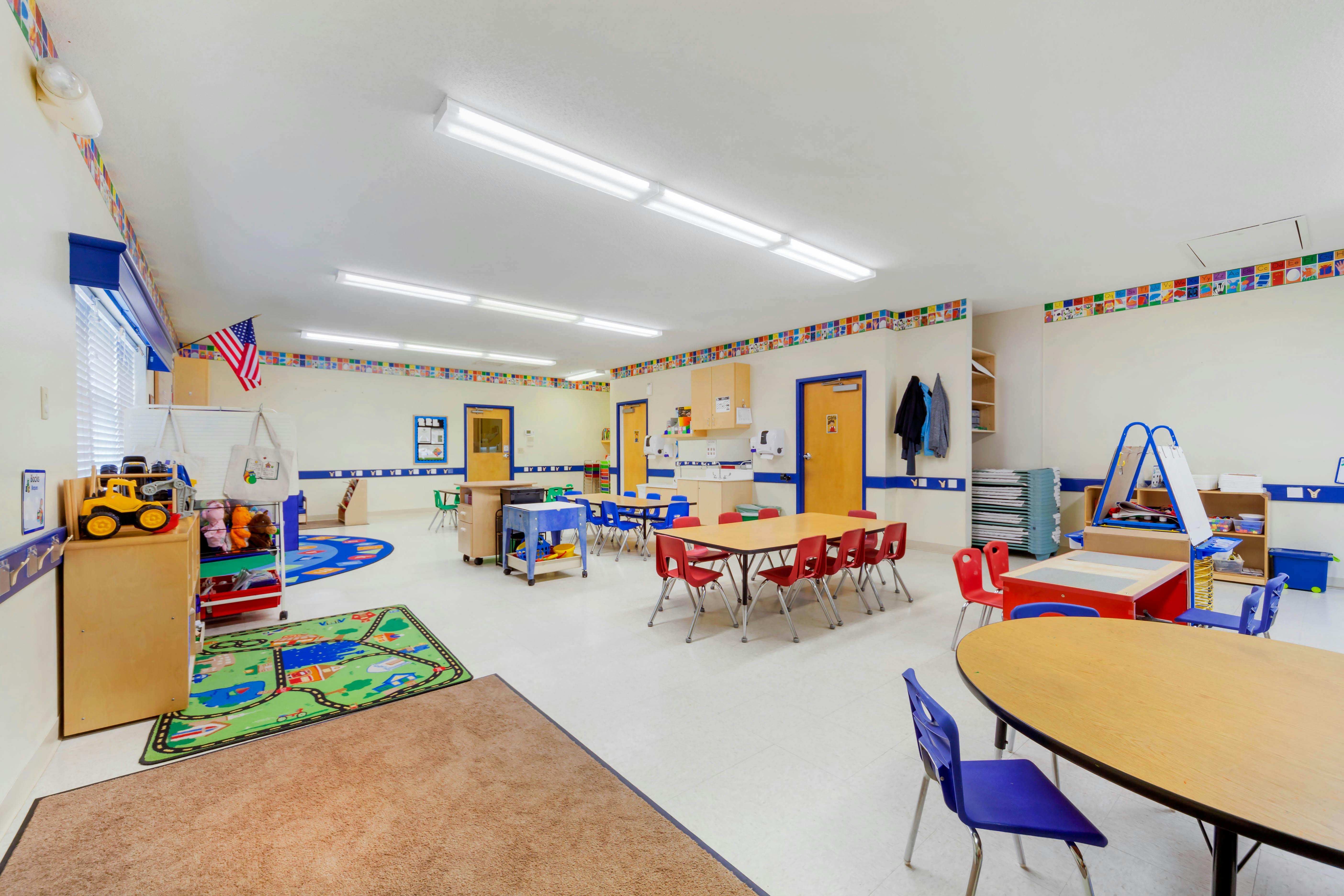 An empty preschool classroom with small tables and chairs