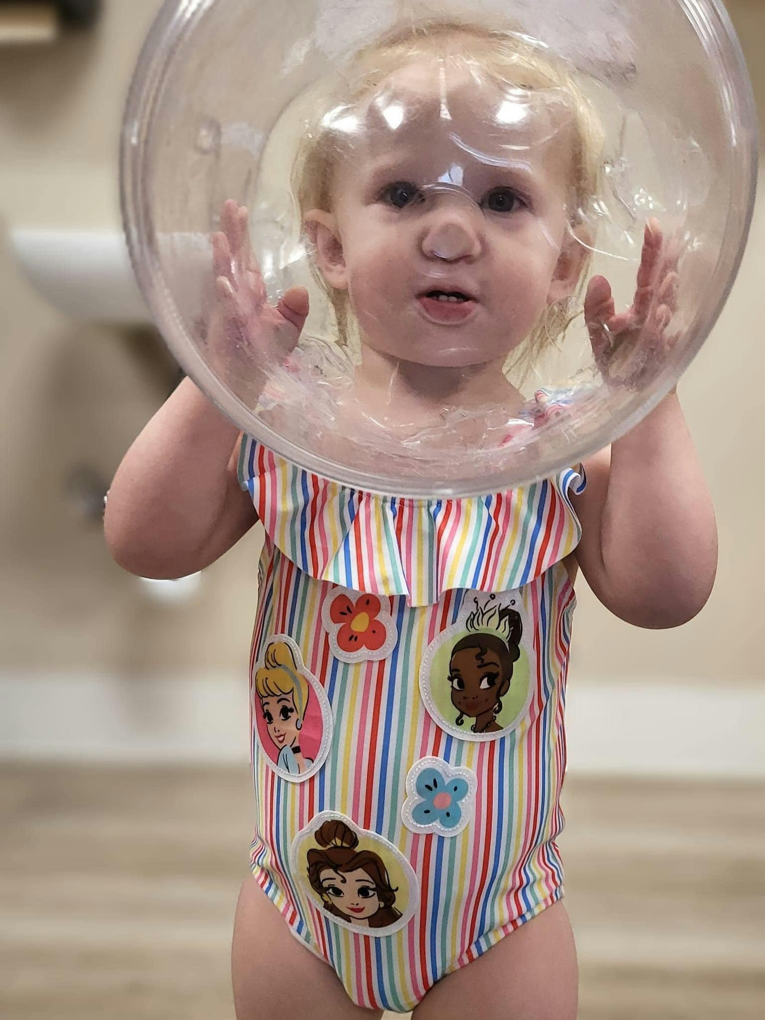 Child wearing a striped swimsuit and a clear plastic bubble over their head