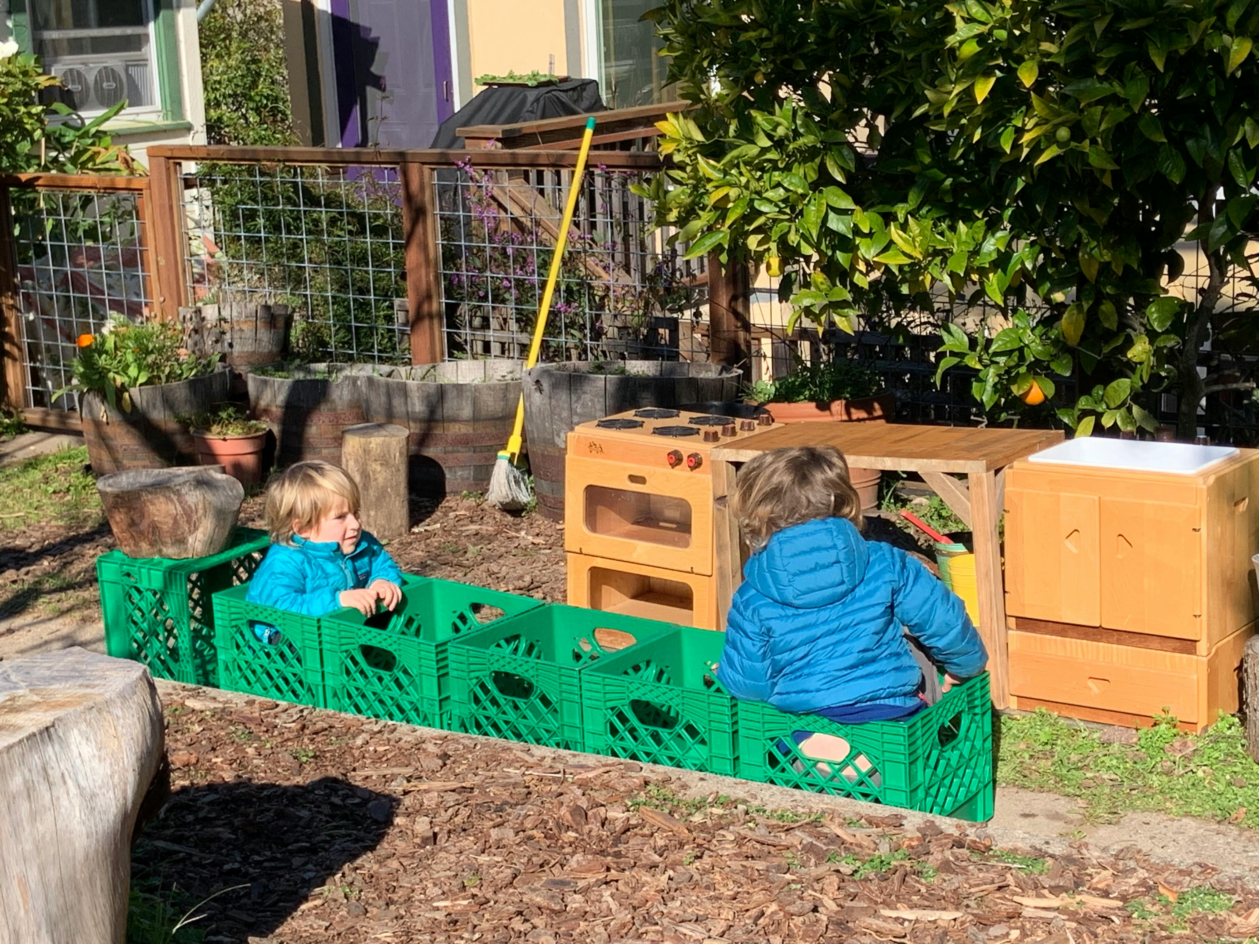 Two children playing with green crates and wooden structures outdoors