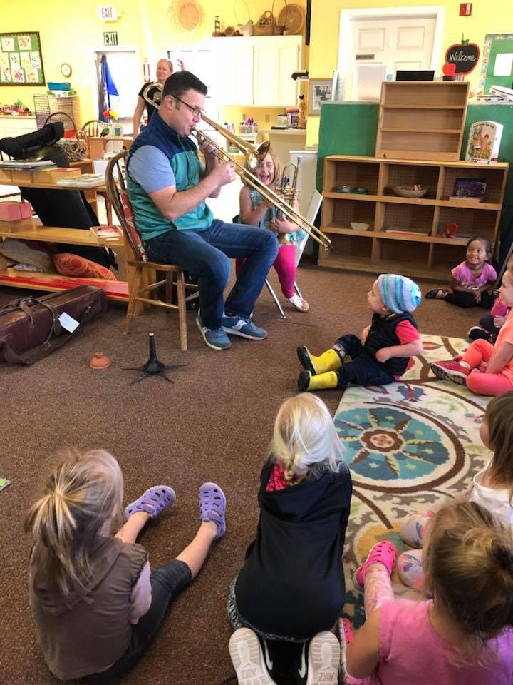 Person playing a trombone for a group of children in a classroom
