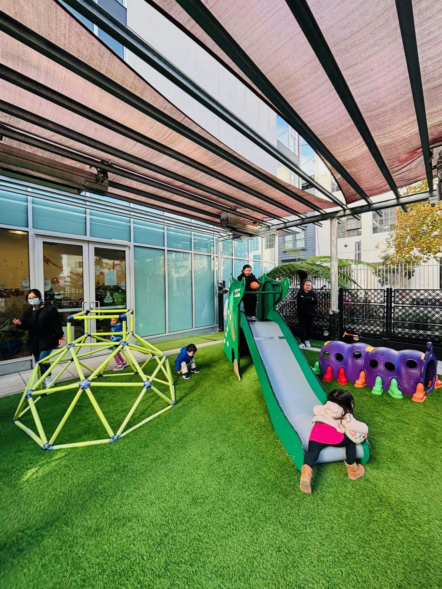 People and children playing on playground equipment on artificial grass