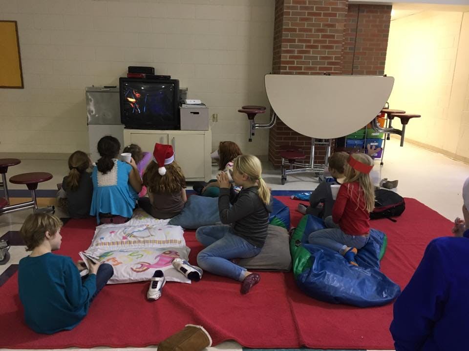 Children sitting on a red mat watching a television